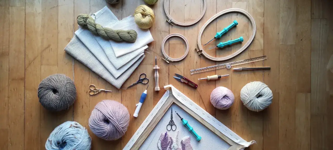 Un lienzo con hilo, aros de bordar, tijeras y herramientas para punch needle, listos para crear arte textil.
