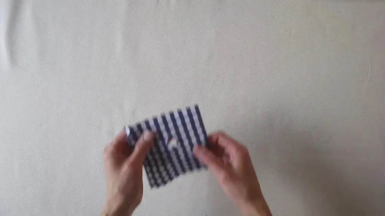 Manos arreglan una ropa con un trozo de tela a cuadros azul y blanco, mostrando cómo reparar una prenda.