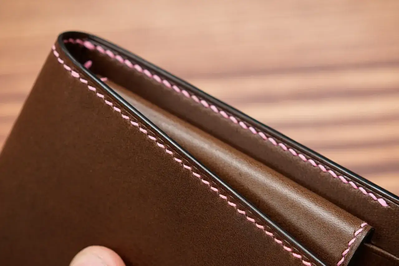 Cartera de cuero marr&oacute;n con costuras rosas hechas a mano, detalle de coser con dos agujas a mano.