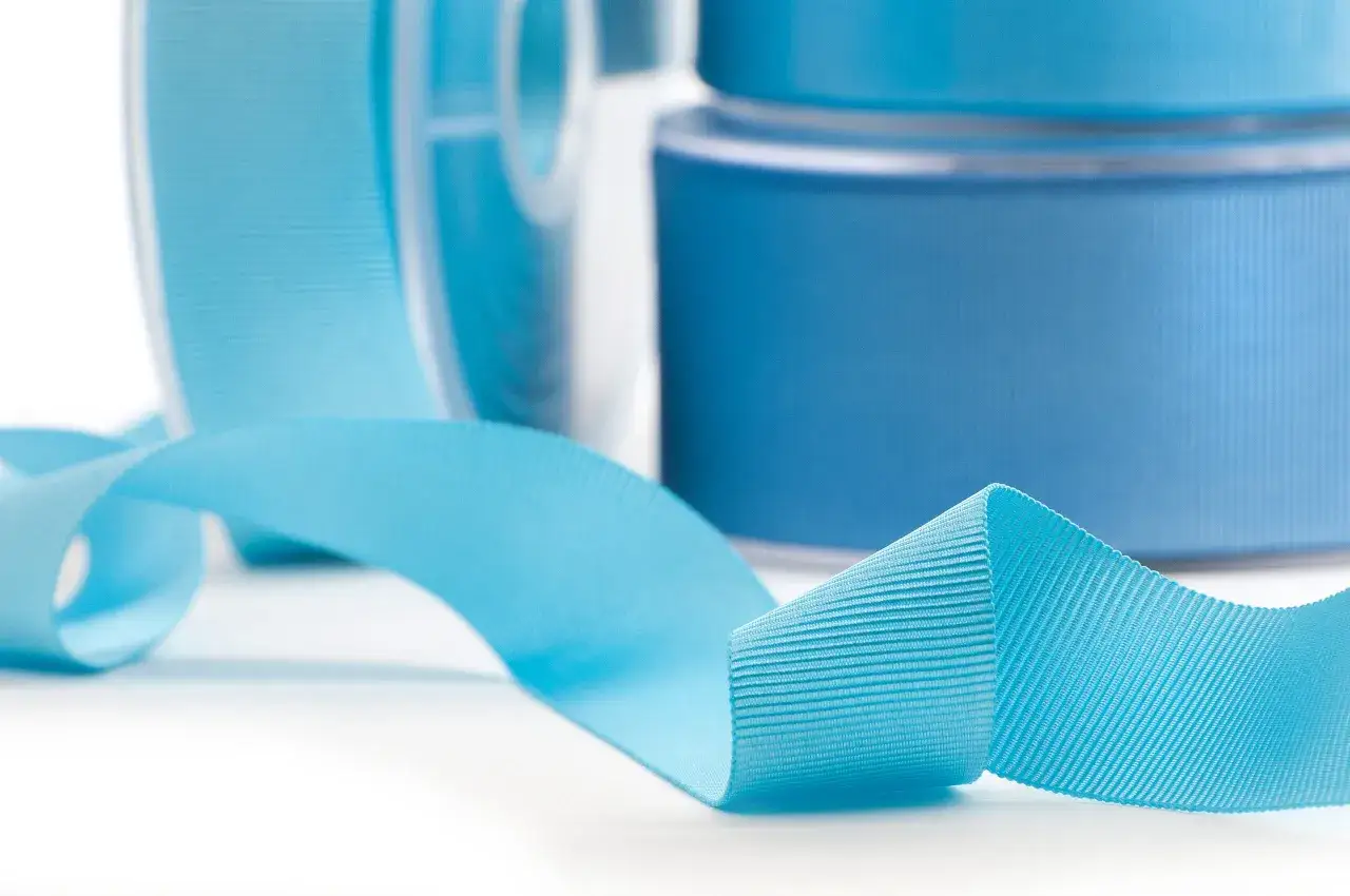 Rollos de diferentes tipos de cintas de tela en tonos azules, con una cinta desplegada en primer plano.