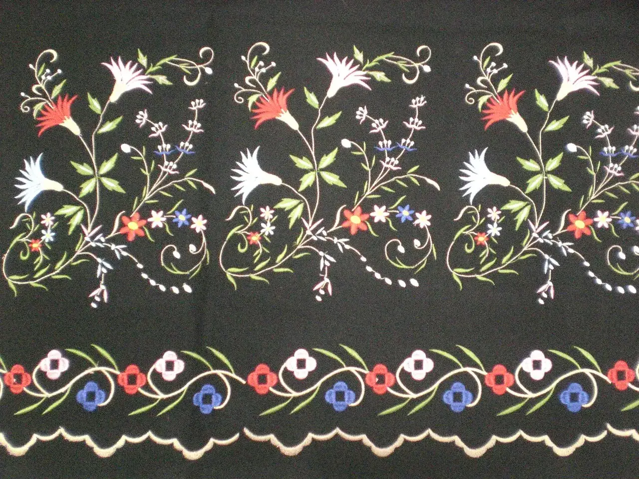 Delicados dibujos para refajos bordados con flores y hojas en tonos rojos, blancos, azules y verdes sobre fondo negro.