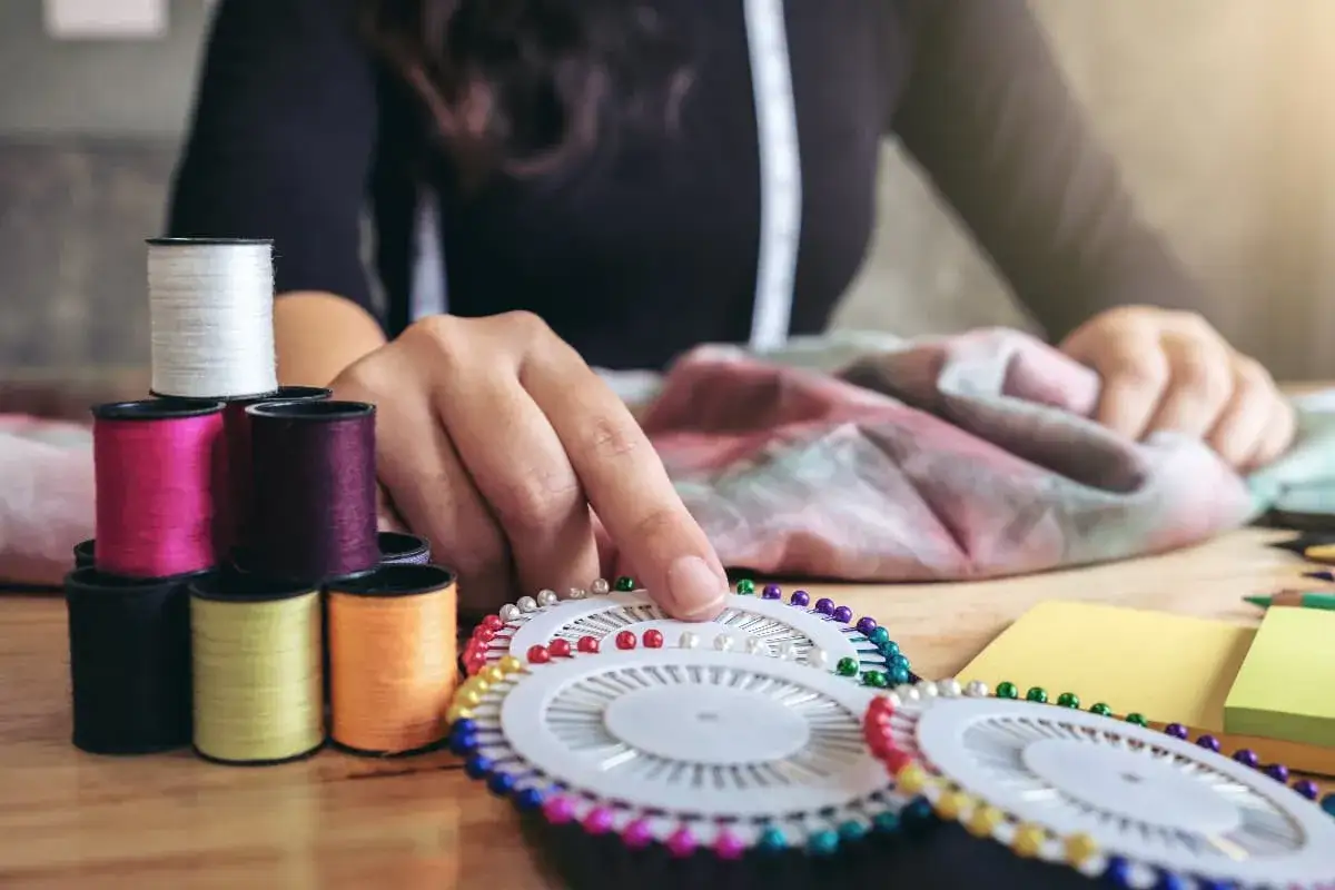Manos preparándose para coser, con hilos de colores, alfileres y tela.