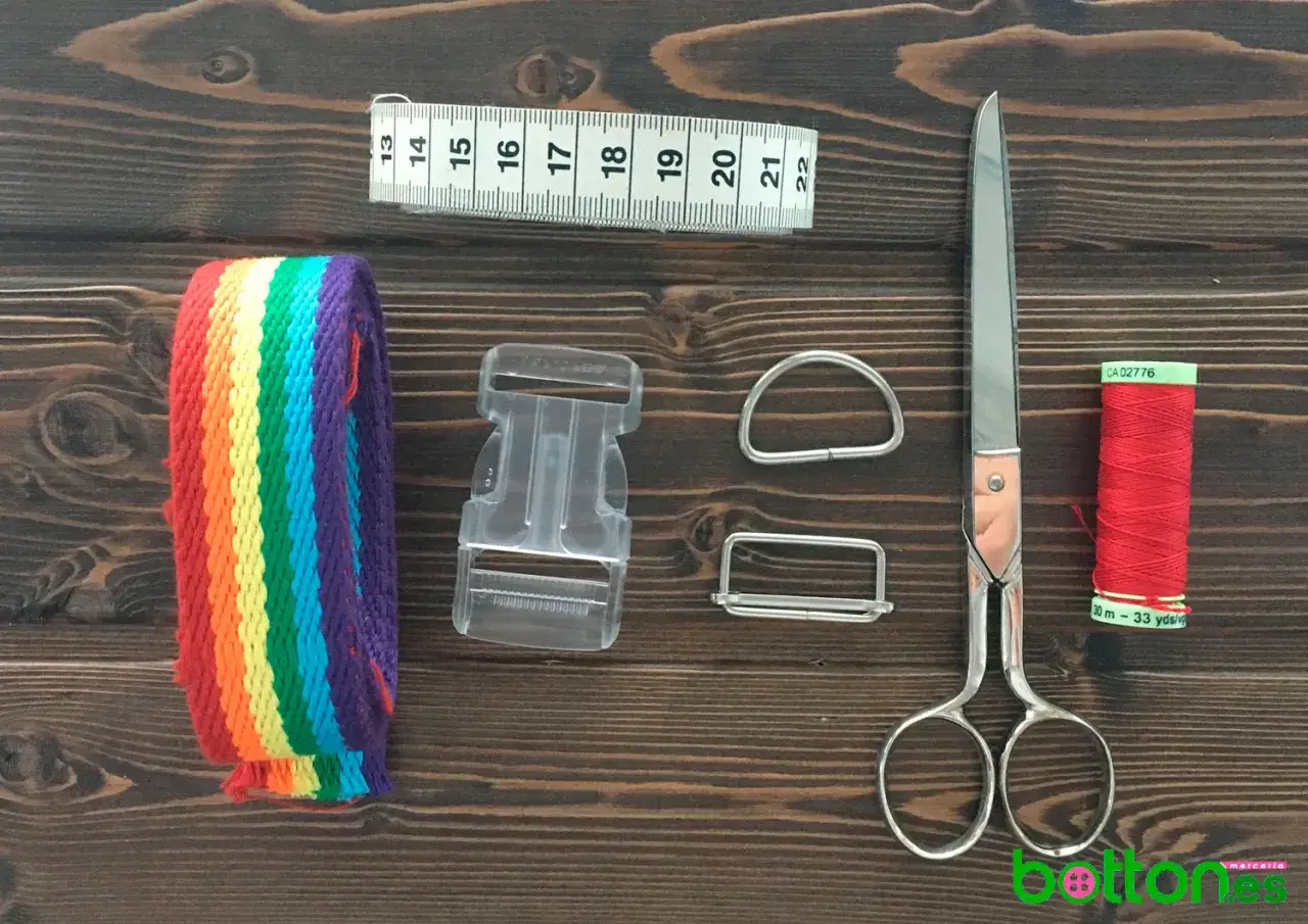 Todo listo para aprender como hacer un collar para perro: cinta arco&iacute;ris, hebilla, anillas, tijeras, cinta m&eacute;trica y hilo rojo.