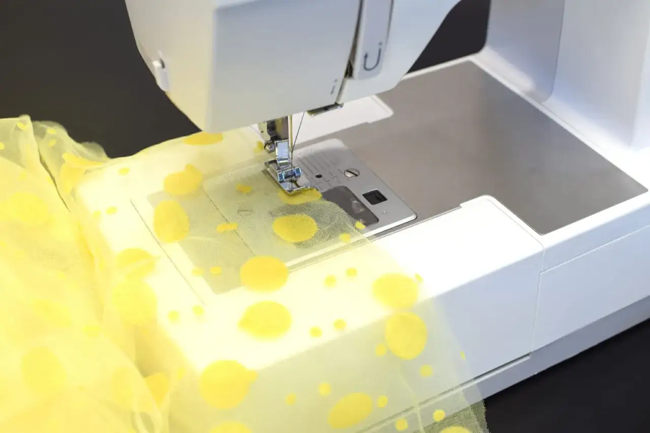 Máquina de coser trabajando con tul amarillo de lunares. Aprende como coser tul a mano con esta imagen de detalle.