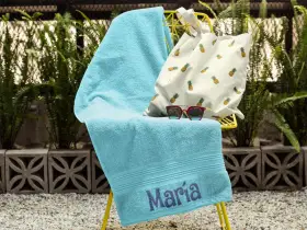 Toalla turquesa con el nombre "María" bordado, lista para la playa.