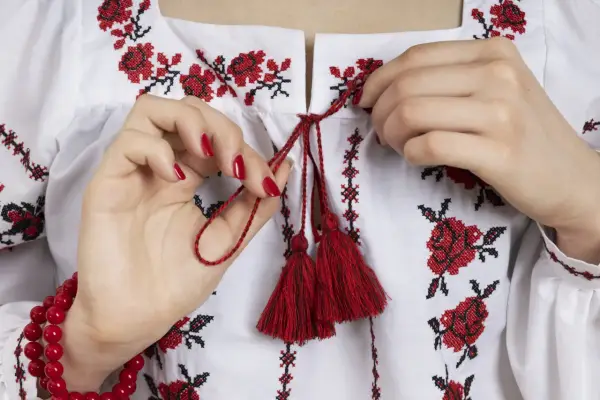 Manos atando cordones rojos en una blusa blanca con **bordado digital** de flores rojas y negras.