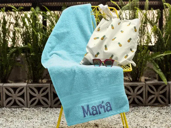Toalla turquesa con el nombre "María" bordado, lista para la playa.