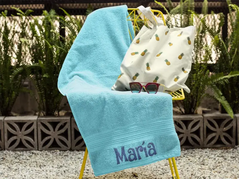 Toalla turquesa con el nombre "María" bordado, lista para la playa.
