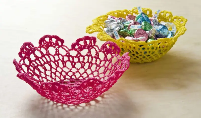 Dos cuencos de ganchillo, uno rosa y otro amarillo lleno de caramelos. Aprende como dar rigidez a una tela para crear estas piezas decorativas.