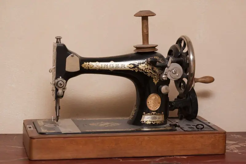 Máquina de coser Singer antigua, pieza clave en la historia de la costura, con detalles dorados y base de madera.
