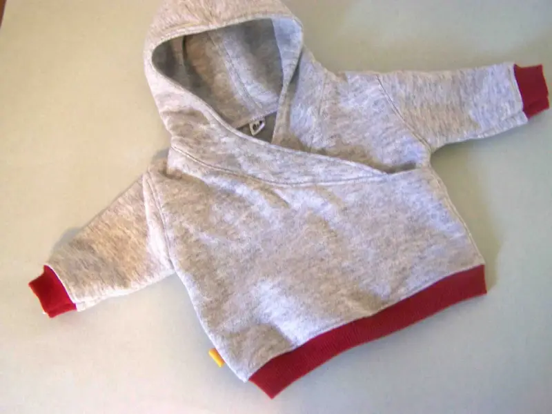 Saco de bebé gris con capucha y puños rojos. Un patrón de saco de bebé con capucha listo para coser.